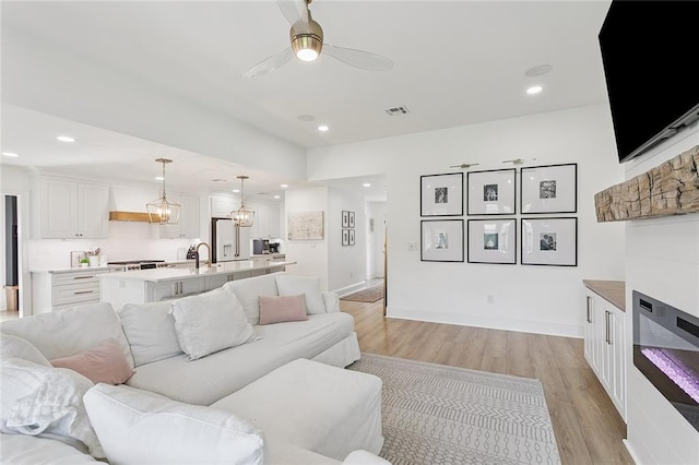 4548 Alphonse Dr, Metairie, LA 70006 - living room featuring light wood-type flooring, a ceiling fan, recessed lighting, a glass covered fireplace, and a chandelier