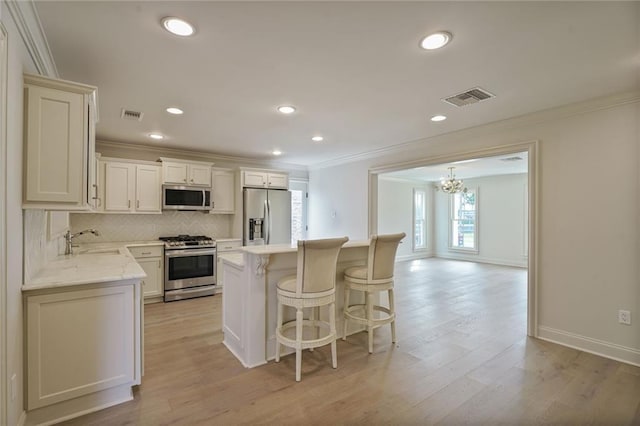 2232 N Starrett Rd, Metairie, LA 70003 - kitchen with stainless steel appliances, crown molding, a chandelier, light wood-type flooring, and a kitchen bar