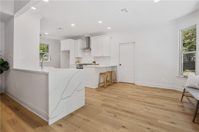 773 Rue Calais, Mandeville, LA 70471 - kitchen with wall chimney range hood, a peninsula, recessed lighting, light wood-style floors, and white cabinetry