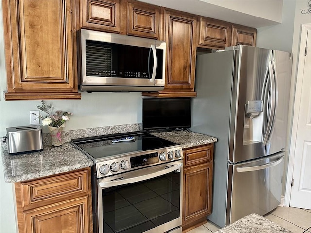 4908 David Dr, Kenner, LA 70065 - kitchen with stainless steel appliances, light tile patterned floors, brown cabinets, and light stone countertops