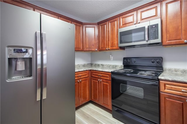 1700 Marseille Dr Unit 16, La Place, LA 70068 - kitchen featuring appliances with stainless steel finishes, light wood-type flooring, brown cabinetry, and a textured ceiling