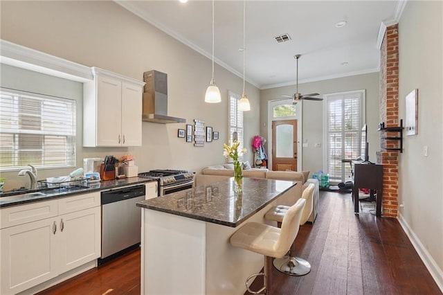 232830 Bienville St, New Orleans, LA 70119 - kitchen featuring appliances with stainless steel finishes, wall chimney range hood, dark wood finished floors, a kitchen island, and dark stone countertops