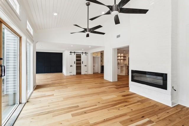 107 Quail St, Slidell, LA 70460 - unfurnished living room featuring a barn door, light wood-style flooring, ceiling fan, recessed lighting, and a glass covered fireplace