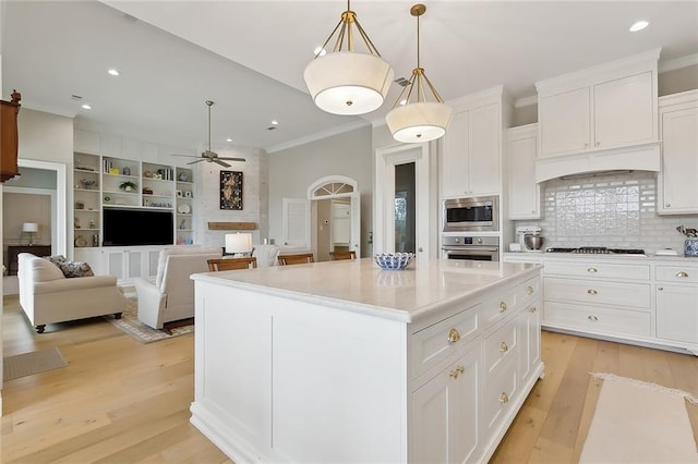 1193 Delta Ln, Covington, LA 70433 - kitchen with appliances with stainless steel finishes, ceiling fan, crown molding, a center island, and white cabinetry
