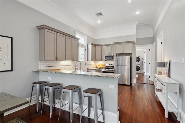 1529 St Philip St, New Orleans, LA 70116 - kitchen with appliances with stainless steel finishes, a peninsula, crown molding, light stone countertops, and decorative backsplash