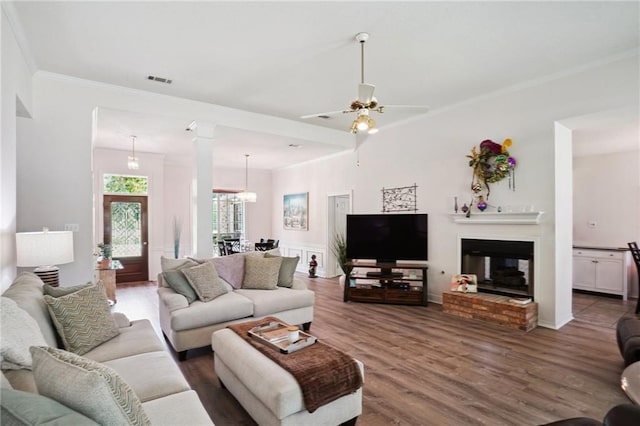 67061 Dolan St, Mandeville, LA 70471 - living room with wood finished floors, ornamental molding, a ceiling fan, a brick fireplace, and decorative columns