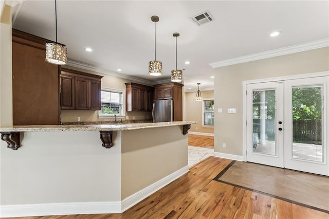4953 Music St, New Orleans, LA 70122 - kitchen with freestanding refrigerator, a kitchen bar, ornamental molding, light wood-type flooring, and dark brown cabinetry