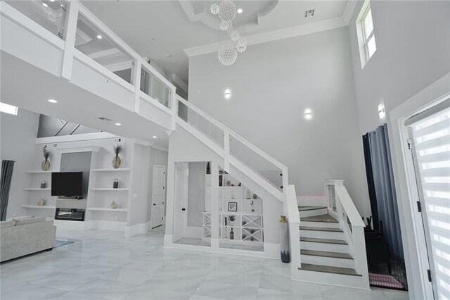 251 Oakmont Dr, New Orleans, LA 70128 - staircase featuring a high ceiling, built in shelves, a chandelier, marble tiled flooring, and ornamental molding