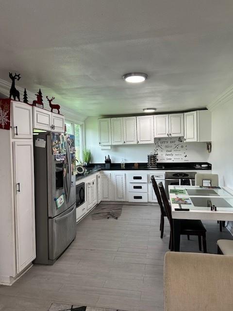 2310 Carlie St, Franklinton, LA 70438 - kitchen with stainless steel refrigerator with ice dispenser, black microwave, white cabinets, dark countertops, and light wood-style flooring