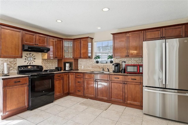 128 Marilyn Dr, Slidell, LA 70461 - kitchen with freestanding refrigerator, black range with electric stovetop, under cabinet range hood, brown cabinetry, and backsplash