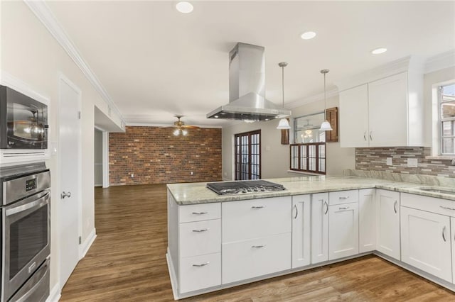 1524 Peach St, Metairie, LA 70001 - kitchen featuring wall chimney range hood, appliances with stainless steel finishes, a peninsula, white cabinets, and ornamental molding