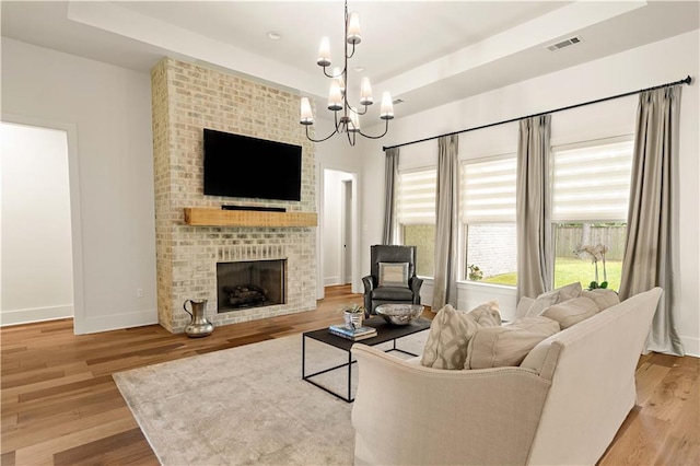 4028 Cypress Point Dr, Covington, LA 70433 - living area with a chandelier, a brick fireplace, a tray ceiling, and light wood-style floors
