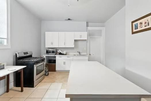 1635 Frenchmen St, New Orleans, LA 70116 - kitchen with appliances with stainless steel finishes, white cabinetry, light countertops, and light tile patterned floors