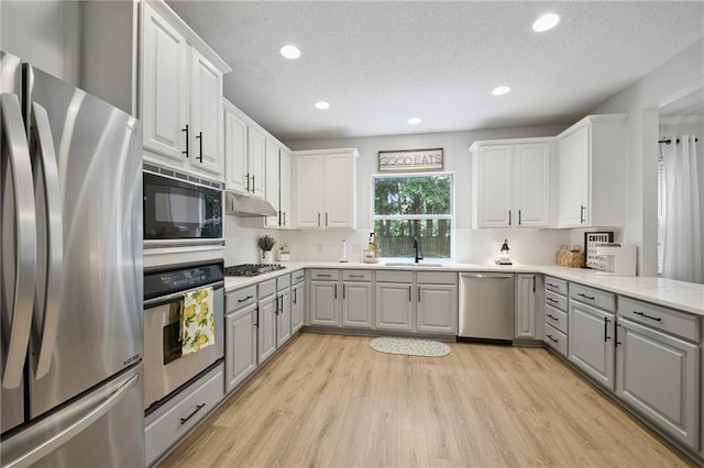 1125 Lori Dr, Slidell, LA 70461 - kitchen with appliances with stainless steel finishes, gray cabinetry, under cabinet range hood, light wood-style flooring, and light countertops