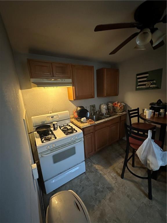 2620-22 Philip St, New Orleans, LA 70113 - kitchen with white range with gas stovetop, under cabinet range hood, a ceiling fan, and brown cabinets
