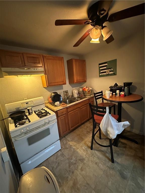 2620-22 Philip St, New Orleans, LA 70113 - kitchen with white range with gas stovetop, under cabinet range hood, a ceiling fan, and brown cabinetry