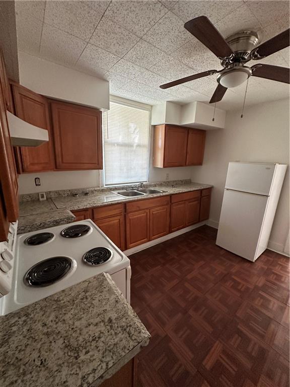 2217 Willow St, New Orleans, LA 70113 - kitchen with white appliances, under cabinet range hood, brown cabinets, ceiling fan, and light countertops