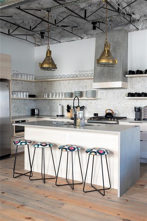 424 S Lopez St, New Orleans, LA 70119 - kitchen featuring open shelves, appliances with stainless steel finishes, backsplash, a breakfast bar, and light wood-style flooring