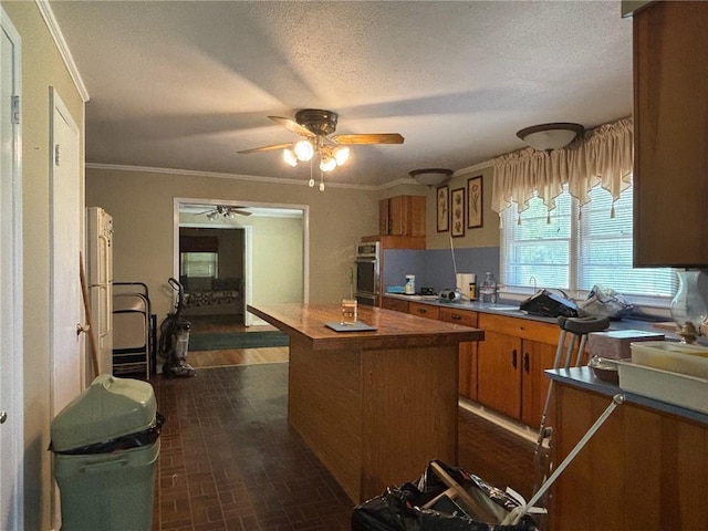 19343 9th Ave, Covington, LA 70433 - kitchen featuring brown cabinetry, stainless steel oven, ceiling fan, a center island, and ornamental molding