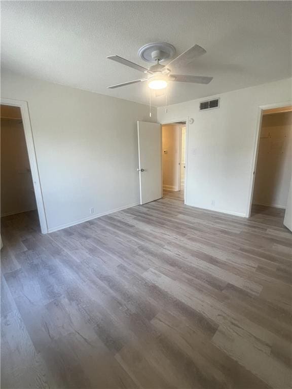3320 N Arnoult Rd Unit 239, Metairie, LA 70002 - unfurnished bedroom with a walk in closet, light wood-style floors, a ceiling fan, a closet, and a textured ceiling