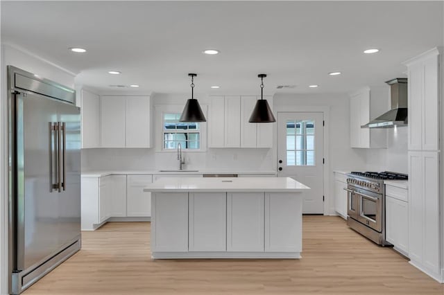 1208 Madison St, Metairie, LA 70001 - kitchen with premium appliances, wall chimney range hood, light countertops, light wood-type flooring, and white cabinets