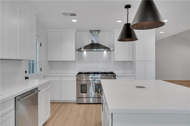 1208 Madison St, Metairie, LA 70001 - kitchen featuring appliances with stainless steel finishes, wall chimney exhaust hood, white cabinets, light countertops, and light wood-type flooring