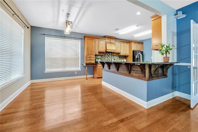 2004 Dierdorff Ct, Slidell, LA 70461 - kitchen featuring black fridge, a breakfast bar, ventilation hood, light wood finished floors, and a peninsula