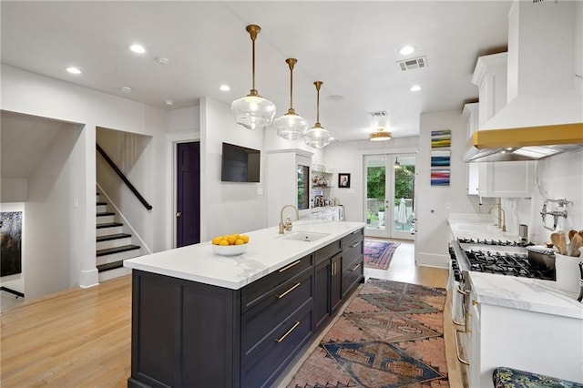 1455 Moss St, New Orleans, LA 70119 - kitchen featuring premium range hood, light wood finished floors, french doors, a kitchen island with sink, and recessed lighting