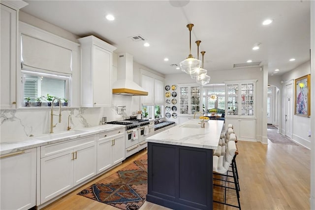 1455 Moss St, New Orleans, LA 70119 - kitchen with custom range hood, range with two ovens, white cabinets, a center island, and light wood-type flooring