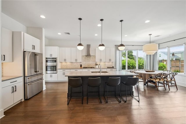 800 Ridgelake Dr, Metairie, LA 70001 - kitchen featuring appliances with stainless steel finishes, wall chimney exhaust hood, a kitchen bar, dark wood-style flooring, and tasteful backsplash
