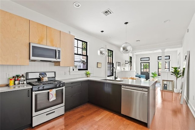 1039-41 Poland Ave, New Orleans, LA 70117 - kitchen with stainless steel appliances, a peninsula, light countertops, light brown cabinetry, and decorative columns