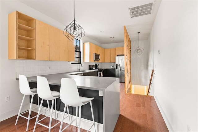 1039-41 Poland Ave, New Orleans, LA 70117 - kitchen with stainless steel appliances, light brown cabinets, a peninsula, light wood-style flooring, and backsplash