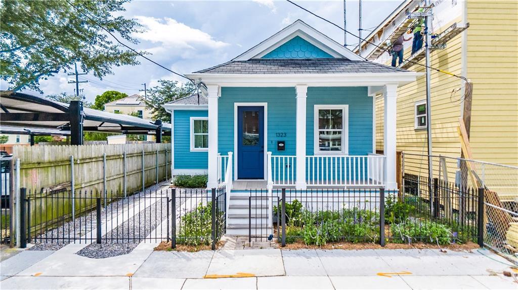 1323 S Rampart St, New Orleans, LA 70113 - shotgun-style home featuring a porch, a shingled roof, a fenced front yard, and a gate