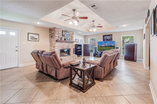 122 Warwick St, La Place, LA 70068 - living area featuring light tile patterned flooring, a textured ceiling, a tray ceiling, a brick fireplace, and ceiling fan