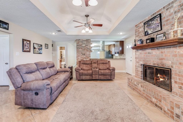 122 Warwick St, La Place, LA 70068 - living room with ceiling fan, a fireplace, a raised ceiling, light tile patterned flooring, and a textured ceiling