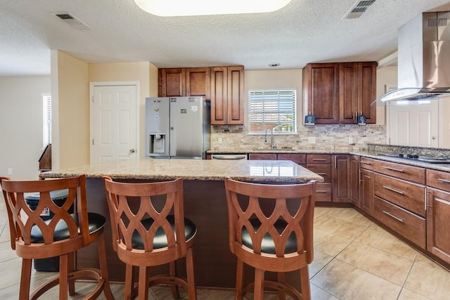 122 Warwick St, La Place, LA 70068 - kitchen with fridge with ice dispenser, wall chimney exhaust hood, tasteful backsplash, a kitchen bar, and light stone countertops