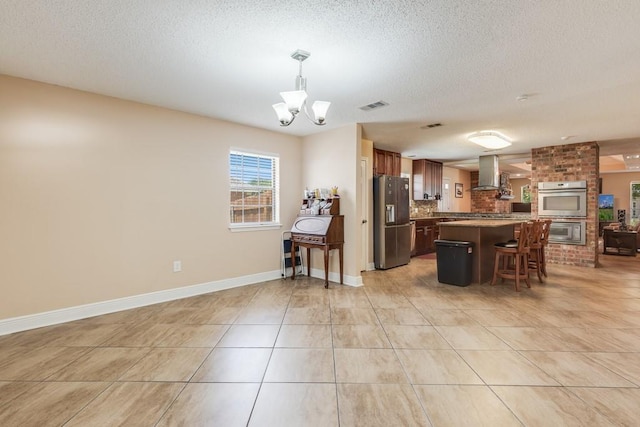 122 Warwick St, La Place, LA 70068 - kitchen featuring stainless steel appliances, wall chimney range hood, light tile patterned flooring, a chandelier, and a kitchen bar