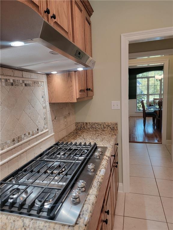 89 Catalpa Trce, Covington, LA 70433 - kitchen with under cabinet range hood, stainless steel gas cooktop, light tile patterned flooring, backsplash, and brown cabinetry