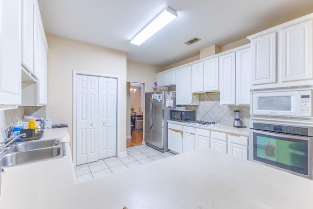 2143 Summertree Dr, Slidell, LA 70460 - kitchen with stainless steel appliances, light tile patterned flooring, white cabinetry, decorative backsplash, and light countertops