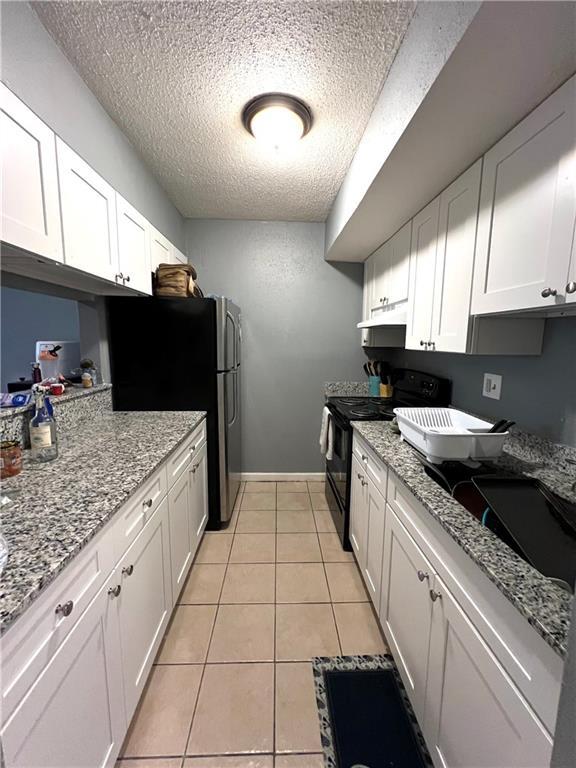 4325 Loire Dr, Kenner, LA 70065 - kitchen featuring black range with electric stovetop, a textured ceiling, white cabinetry, freestanding refrigerator, and light tile patterned floors
