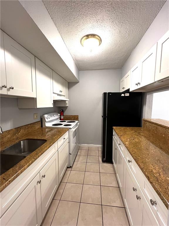 4325 Loire Dr, Kenner, LA 70065 - kitchen with white range with electric cooktop, under cabinet range hood, a textured ceiling, white cabinets, and freestanding refrigerator