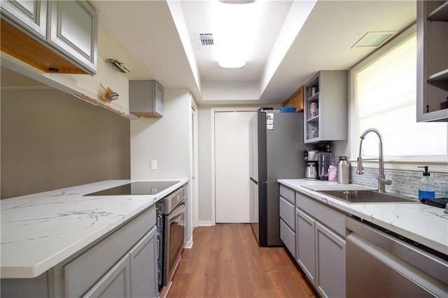 2137 Carmel Valley Dr, La Place, LA 70068 - kitchen with appliances with stainless steel finishes, open shelves, gray cabinets, wood finished floors, and decorative backsplash