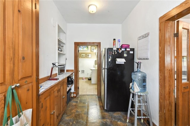 1815 S White St, New Orleans, LA 70125 - kitchen with freestanding refrigerator, brown cabinetry, light countertops, and dark stone finish floors