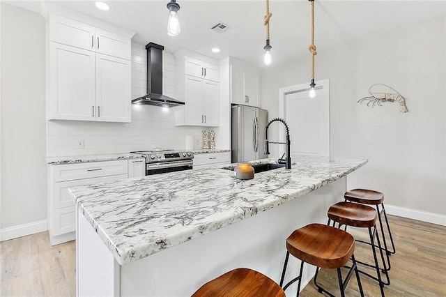4320 Alba Rd, New Orleans, LA 70129 - kitchen with wall chimney exhaust hood, stainless steel appliances, light wood-style flooring, an island with sink, and white cabinets