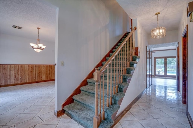 119 Gondrella Dr, Belle Chasse, LA 70037 - stairs with a chandelier, tile patterned floors, a textured ceiling, wood walls, and wainscoting