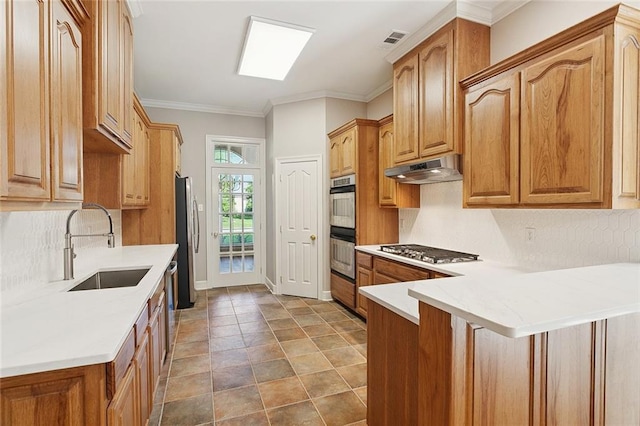 319 Red Maple Dr, Mandeville, LA 70448 - kitchen featuring appliances with stainless steel finishes, under cabinet range hood, tasteful backsplash, a peninsula, and light countertops
