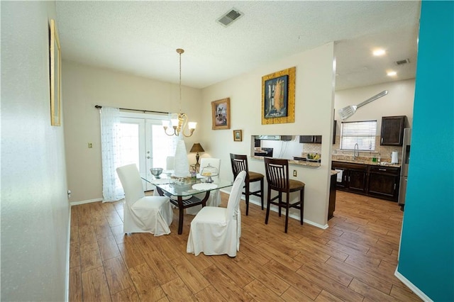 157 Barnes Ct, Gretna, LA 70056 - dining room featuring light wood-style floors, a chandelier, a textured ceiling, and french doors