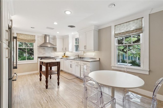 1338 Fern St, New Orleans, LA 70118 - kitchen with wall chimney exhaust hood, healthy amount of natural light, light wood-type flooring, white cabinets, and recessed lighting
