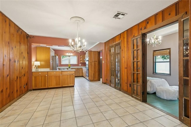 202 Amelia St, Destrehan, LA 70047 - kitchen featuring a chandelier, wood walls, brown cabinetry, a peninsula, and stainless steel appliances