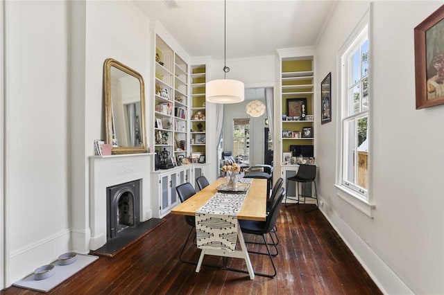 1123 Cadiz St, New Orleans, LA 70115 - dining area with dark wood-style flooring, built in shelves, ornamental molding, and a fireplace with raised hearth